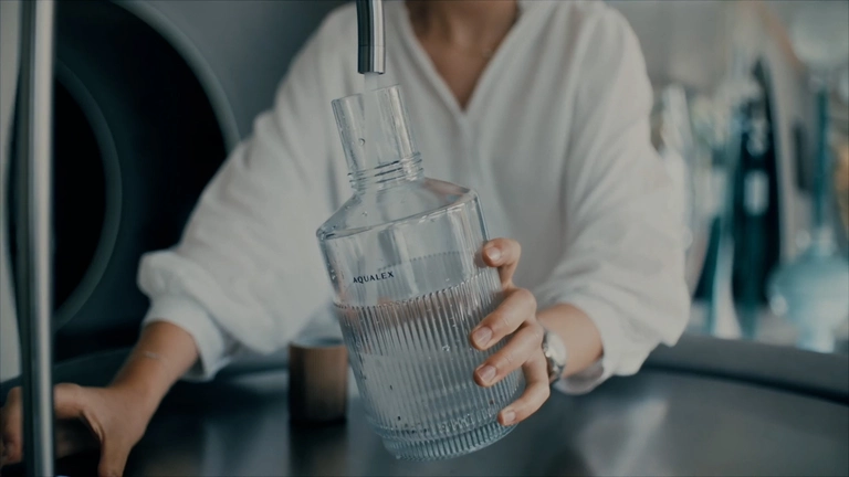 Frau zapft Wasser in Glasflasche am Wasserhahn